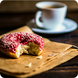 donut croqué posé sur papier kraft et tasse de café en second plan.